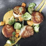 a black plate topped with scallops and vegetables.