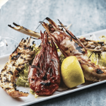 a plate of food with shrimp, lemon and a glass of wine.