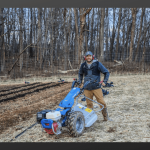 a man standing next to a blue tractor in a field.
