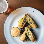 a white plate topped with food next to a glass of beer.
