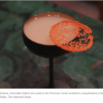 a glass with a drink in it sitting on a table.