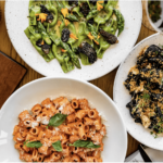 a table topped with plates of food and a bowl of pasta.