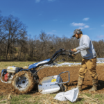 a man standing next to a plow in a field.