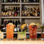a row of different types of cocktails on a bar.