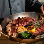 a man holding a large metal pan filled with meat.