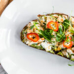 a white plate topped with a piece of bread covered in veggies.