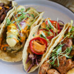 three tacos on a plate with a glass of water.