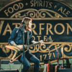 a man playing a guitar in front of a sign.