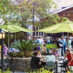 a group of people sitting at tables under umbrellas.