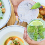 a person holding a drink in front of a plate of food.