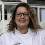 a woman in a chef's coat standing in front of a house.