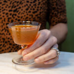 A person in a leopard print top holding a star-patterned glass filled with amber liquid at a table.