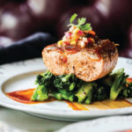 A plate of salmon, broccoli and wine on a table.