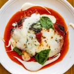 A plate of lasagna with sauce and basil on a wooden table.